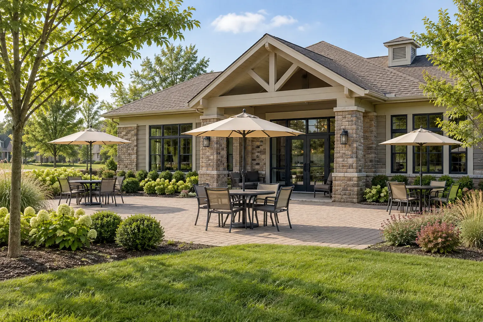 Clubhouse paver patio with tables and umbrellas beside a lawn and planting beds