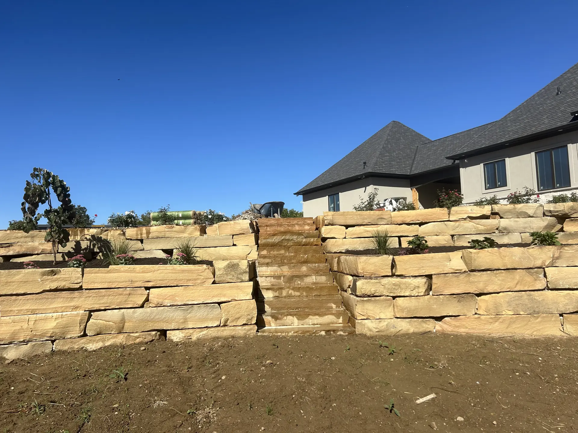 Tiered sandstone slab retaining walls with center steps and new plantings below a home in Indianapolis