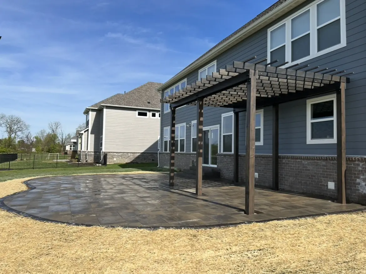 Gray paver patio with a dark-stained pergola along the back of a two-story home in Indianapolis