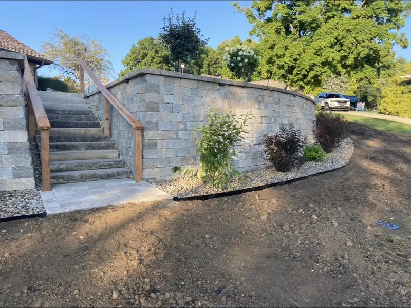 Block retaining wall with stone steps and wood handrails beside a new planting bed