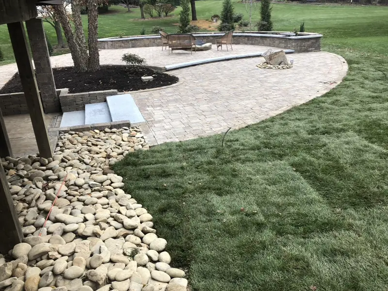 Curved paver patio with a seat wall, river rock bed and new sod in Indianapolis