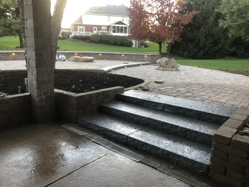 Stone steps from a paver patio with a block planter around a tree in Indianapolis