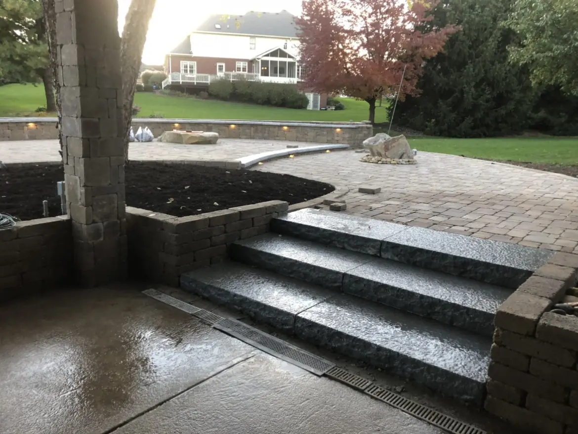 Stone steps from a paver patio with a block planter around a tree in Indianapolis