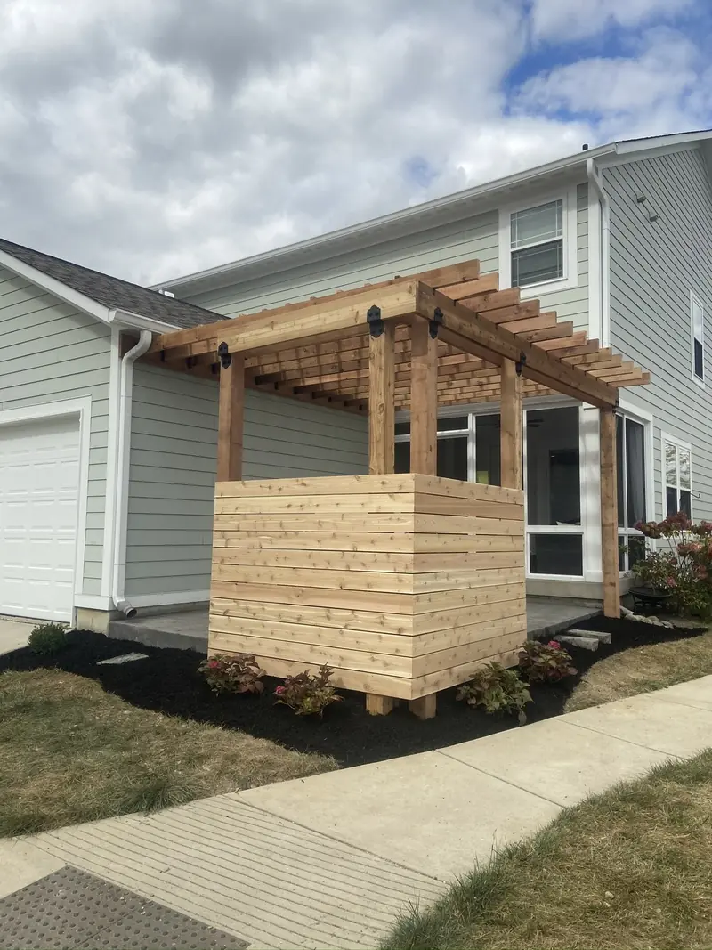 Cedar privacy screen with a pergola top beside fresh mulch beds