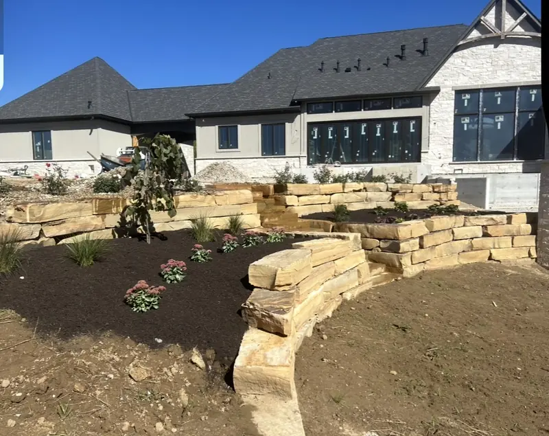 Tiered natural stone walls with new plantings in front of a large home in Carmel, IN