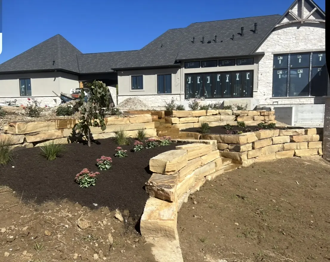 Tiered natural stone walls with new plantings in front of a large home