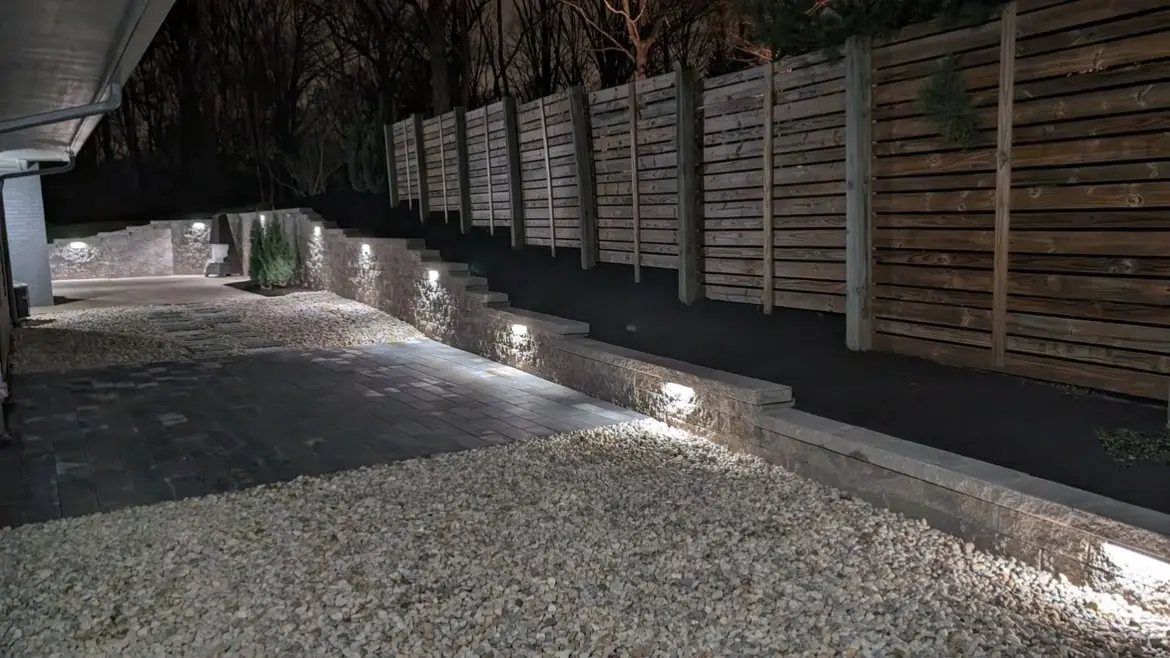 Wall lights along a low retaining wall and paver path at night in Indianapolis