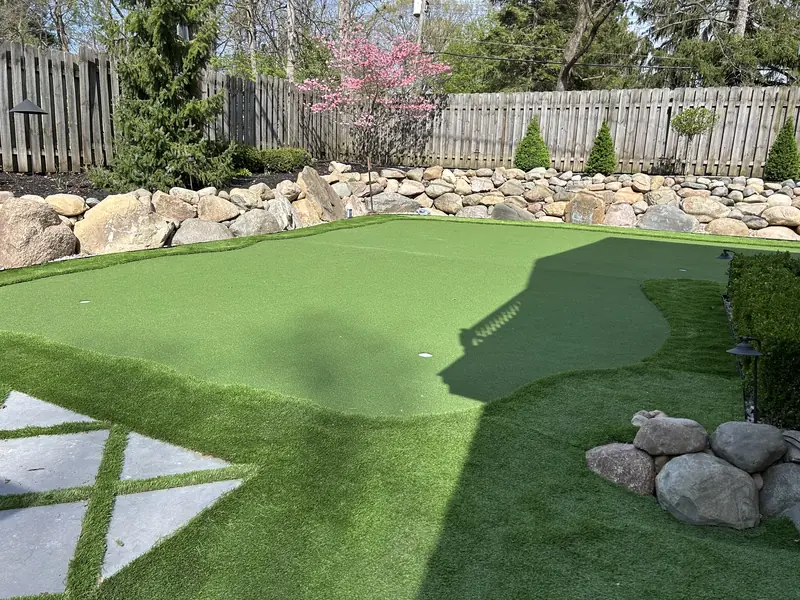 Backyard putting green framed by boulders and turf-joint pavers