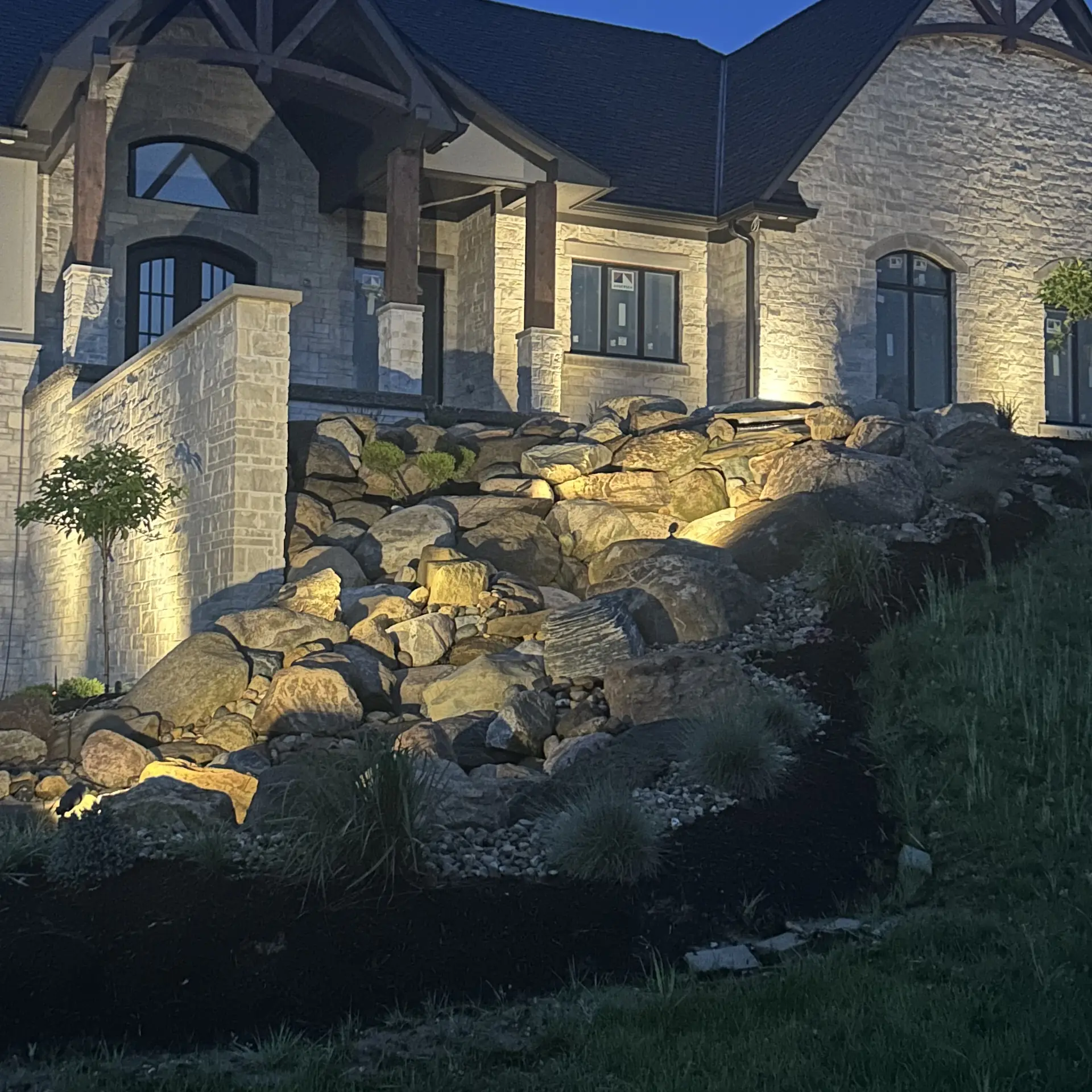 Warm uplighting on a stone home and boulder slope at dusk