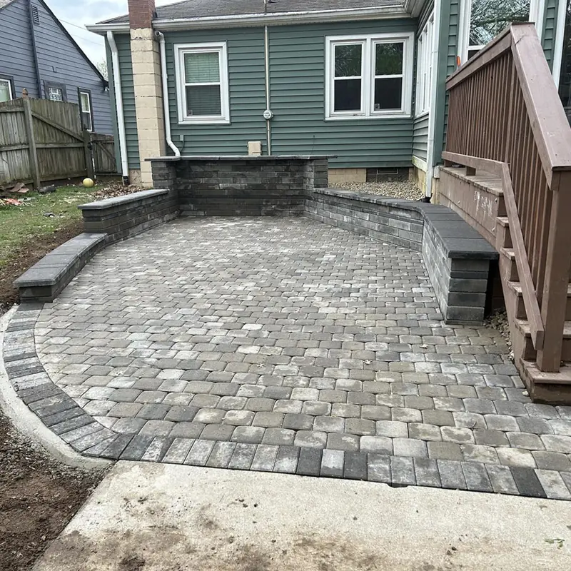 Curved paver patio with seat walls beside deck stairs